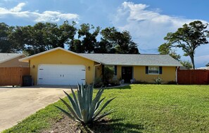 A single-story yellow house with a garage, surrounded by a well-maintained lawn and trees. - Ormond Beach Oasis (Ormond Beach)