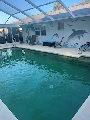 An indoor swimming pool with a dolphin mural, lounge chairs, and a palm tree design on the wall. - Ormond Beach Oasis (Ormond Beach)