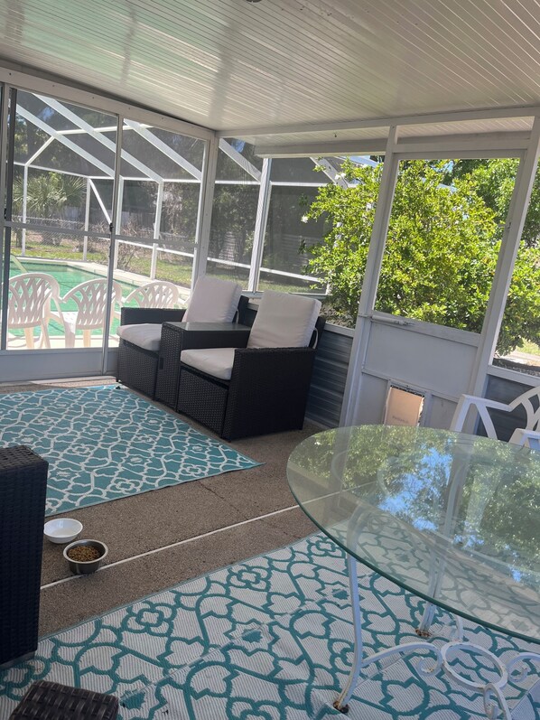 A covered patio area with a glass table, wicker furniture, and a view of a swimming pool. - Ormond Beach Oasis (Ormond Beach)