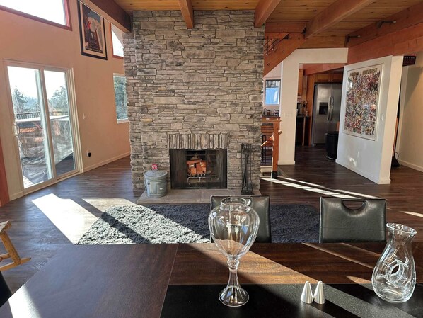 A spacious living room with a stone fireplace, a dining table with a wine glass, and a view of the backyard through large sliding doors.