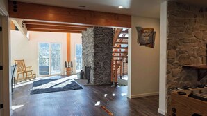 A spacious room with a stone fireplace, wooden beams, and a view of the outdoors. - The Grateful Den - Hot tub, game room (Big Bear Lake)