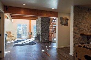 A spacious room with a stone fireplace, wooden beams, and a view of the outdoors.