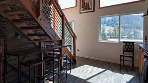 A wooden staircase, a dining area with a table and chairs, and a large window with a view of trees. - The Grateful Den - Hot tub, game room (Big Bear Lake)