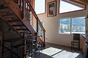 A wooden staircase, a dining area with a table and chairs, and a large window with a view of trees.