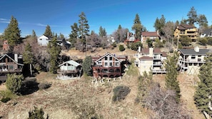 A residential area with multiple houses, some with balconies and decks, surrounded by trees and a hilly landscape.