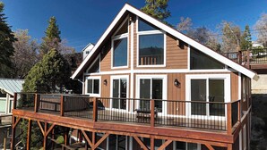 A two-story wooden house with a balcony, large windows, and a metal railing. - The Grateful Den - Hot tub, game room (Big Bear Lake)