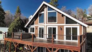A two-story wooden house with a balcony, large windows, and a metal railing.
