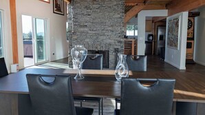 A dining area with a stone fireplace, wooden beams, and a view of the outdoors. - The Grateful Den - Hot tub, game room (Big Bear Lake)