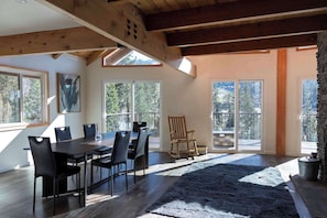 A dining area with a wooden table and chairs, large windows, and a stone fireplace.