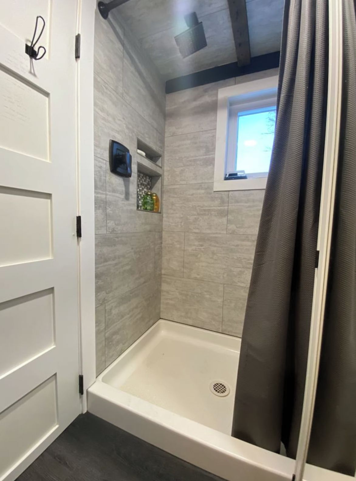 Une douche avec une fenêtre, une étagère pour les articles de toilette et une porte avec une poignée.