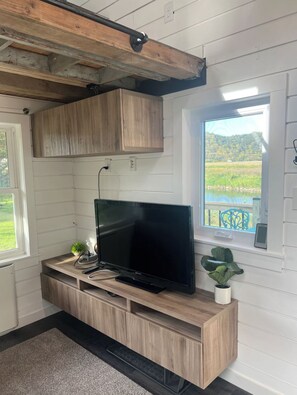 Ein Zimmer mit Fernseher auf einer Holzkabine, einem Fenster mit Blick auf Grünflächen und einer Decke mit sichtbaren Holzbalken.