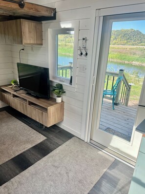 A modern kitchen with a built-in TV, a small plant, and a view of a lake through a sliding door. - Tiny home on the Upper iowa river (Dorchester)