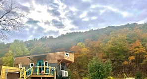 Eine Holzhütte mit Balkon, umgeben von Herbstlaub und bewölktem Himmel.