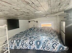 A bedroom with a bed, a TV mounted on the wall, a window with blinds, and a built-in wardrobe. - Tiny home on the Upper iowa river (Dorchester)