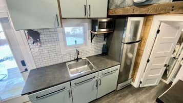 A kitchen with a sink, cabinets, a microwave, and a refrigerator.