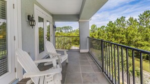 Eine überdachte Veranda mit weißen Stühlen, einem Geländer und Blick auf Bäume.