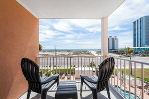 A balcony with two chairs, a pool, and a view of the beach and buildings. - 🪸🌴Beach Views + Across from Gulf State Park | Grand Beach Resort 310 (Gulf Shores)