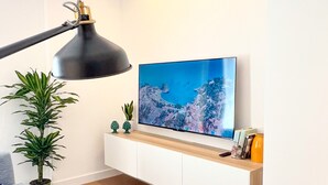 A modern living room with a flat-screen TV, a black floor lamp, a grey sofa, and a wooden cabinet. - April Suites Apartments - Suite 1, Amber (Palermo)