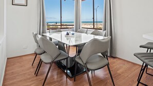 A dining area with a table and chairs, large windows with a beach view, and a framed picture on the wall. - Marina by the Sea | Ocean Reef Luxury 4 Bed + study | Marina & Ocean Views (Ocean Reef)