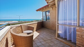 A balcony with wicker furniture, a view of the beach, and a large window with curtains. - Marina by the Sea | Ocean Reef Luxury 4 Bed + study | Marina & Ocean Views (Ocean Reef)