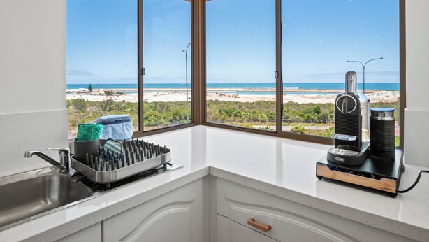 A kitchen with a view of the beach, a coffee maker, and a dish rack. - Marina by the Sea | Ocean Reef Luxury 4 Bed + study | Marina & Ocean Views (Ocean Reef)