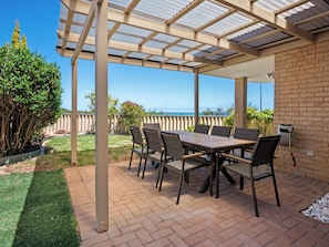 Une terrasse couverte avec une table et des chaises, un mur en briques et une vue sur l’océan.