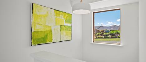A room with a large abstract painting, a window with a view of greenery and buildings, and a white ceiling.