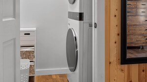A laundry room with two stacked washing machines, a white door, and wooden paneling on the walls. - Bear's Den (Washington Township)