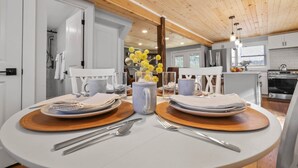 A dining area with a round table set for two, a vase with yellow flowers, and a kitchen in the background. - Bear's Den (Washington Township)