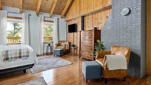 A bedroom with a bed, a wooden ceiling, a gray brick wall, a TV, and a wooden dresser. - Bear's Den (Washington Township)