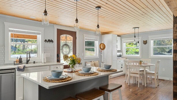 A kitchen with a central island, wooden flooring, pendant lighting, and large windows. - Bear's Den (Washington Township)