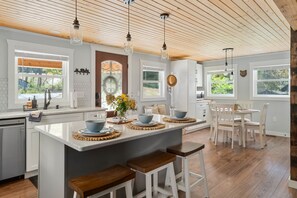 A kitchen with a central island, wooden flooring, pendant lighting, and large windows.