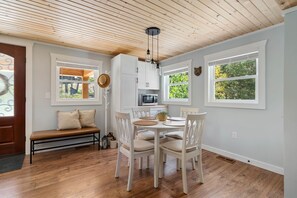 A dining area with a wooden table and chairs, a bench, and a kitchen in the background.