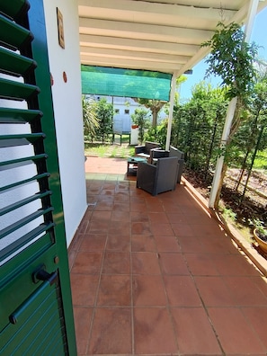 Un patio cubierto con suelo de baldosas, mobiliario exterior y una sombrilla verde.
