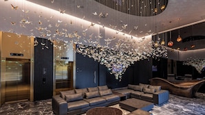 A modern lobby with a large seating area, a reception desk, and a unique ceiling installation of hanging lights. - Hotel Cube (Bar)