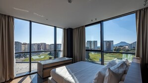 A modern hotel room with large windows, a bed, a bench, and a view of the cityscape. - Hotel Cube (Bar)