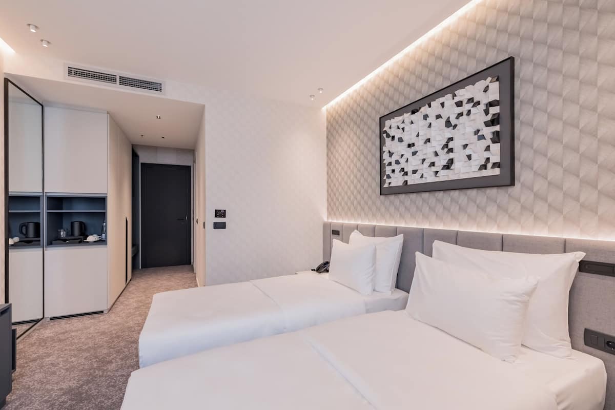 A hotel room with two beds, a minibar, a large mirror, and a geometric wall art piece.