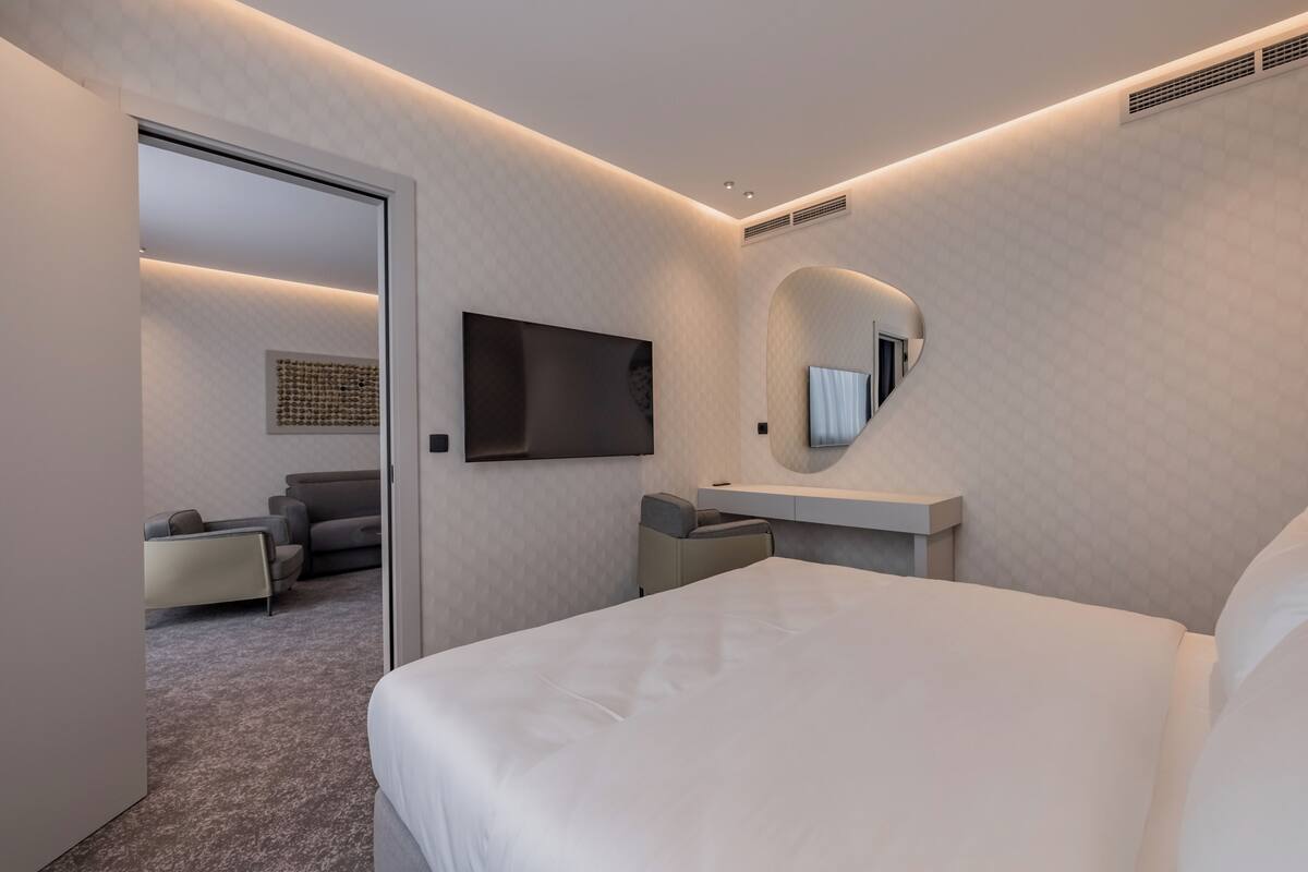 A modern hotel room with a large bed, a flat-screen TV mounted on the wall, a bedside table, and a mirror.