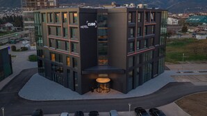 A modern hotel with a glass facade, a prominent 'CUBE HOTEL' sign, and a view of mountains in the background. - Hotel Cube (Bar)