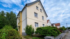 Ein mehrgeschossiges Wohnhaus mit flachem Dach, umgeben von Grünflächen und einem gepflasterten Weg.