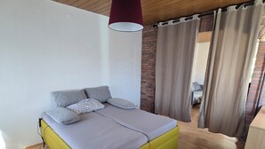Ein modernes Schlafzimmer mit Holzboden, einem Bett mit gelbem Gestell, grauer Bettwäsche und einer roten Pendelleuchte.