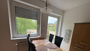 Ein Essbereich mit einem runden Tisch, Stühlen, einer Topfpflanze und Blick durch die Fenster.