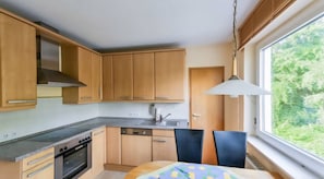 Een keuken met houten kasten, een fornuis, een gootsteen en een eethoek met een tafel en stoelen.