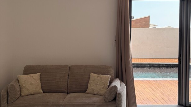 Ein modernes Wohnzimmer mit einer Couch, einem runden Tisch, einem Deckenventilator und Blick auf einen Swimmingpool durch eine Schiebetür.