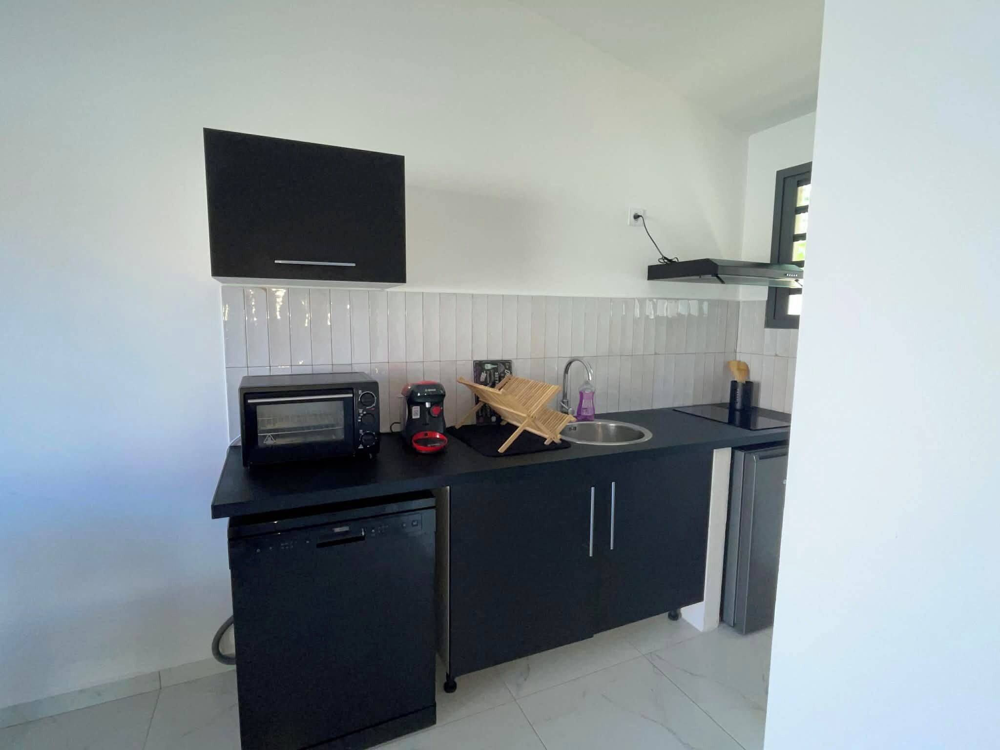 A compact kitchen with a built-in microwave, a small refrigerator, a sink, and a black cabinet.