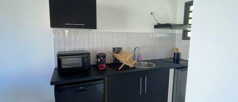 A compact kitchen with a built-in microwave, a small refrigerator, a sink, and a black cabinet.