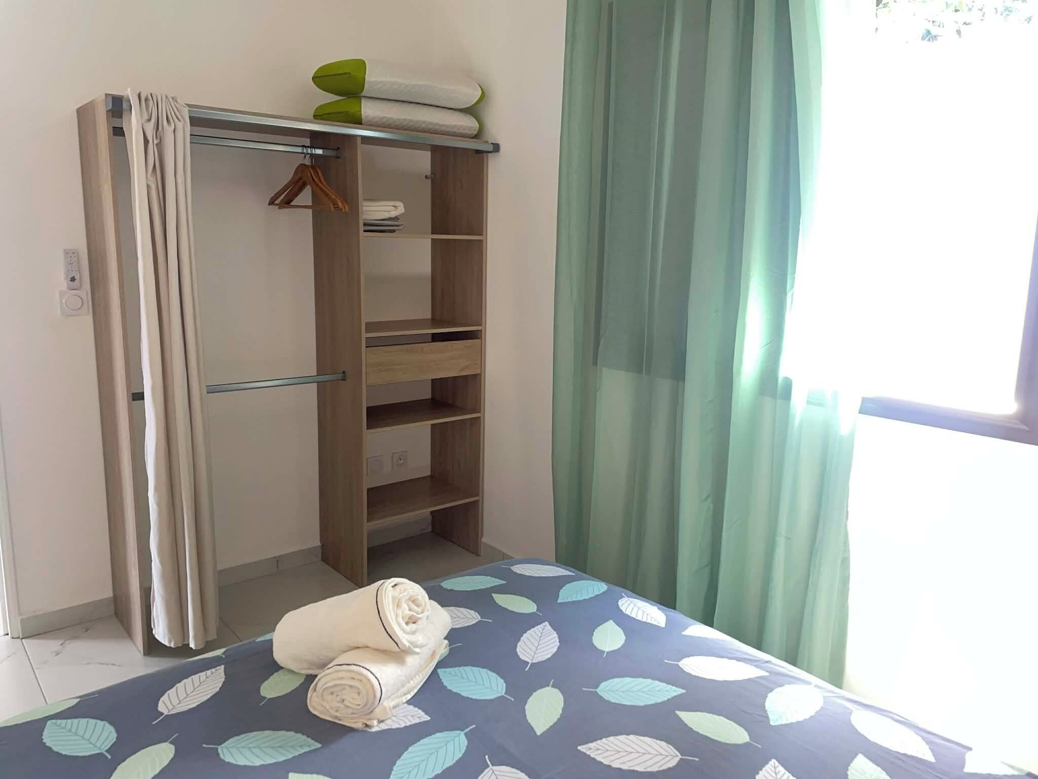 Un dormitorio con cama, armario y ventana con cortinas.