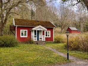 Ett rött trähus med en veranda, en liten trappa och en lyktstolpe, placerat i en naturskön miljö.
