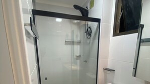 Ein modernes Badezimmer mit einer gläsernen Duschkabine, Toilette und einem Waschbecken mit Natursteinplatte.