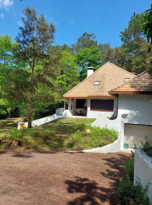 Una casa con techo de tejas, garaje y jardín ajardinado con árboles y arbustos.